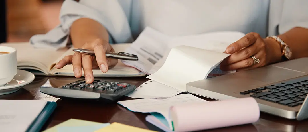 Mujer con papeles y laptop usando una calculadora